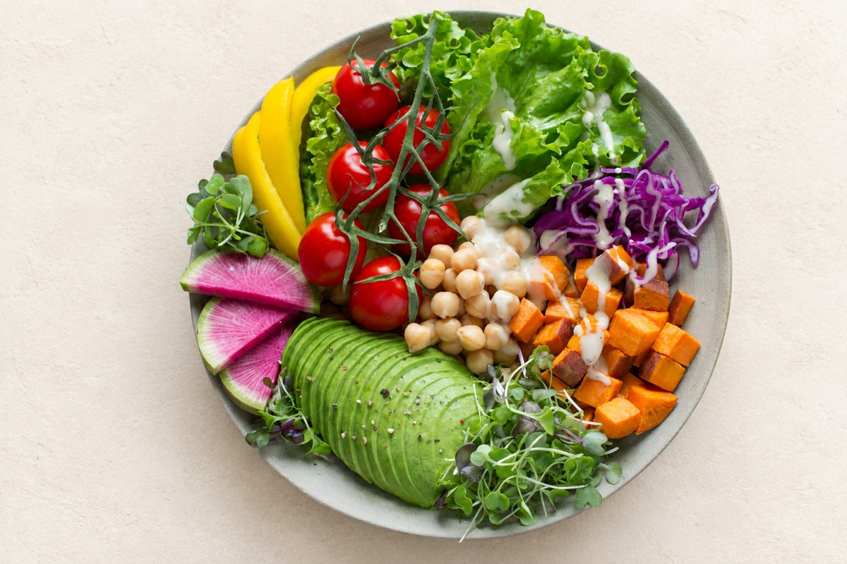 A bowl of colorful vegetables, avocado, and chickpeas on a warm cream surface